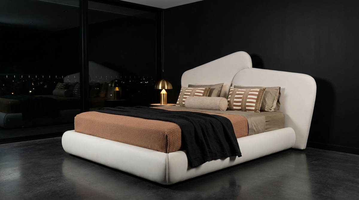 A modern low-profile platform bed with a curved, sculptural headboard and footboard in white leather, styled with a textured tan quilt, striped beige pillows, and a black throw blanket, set in a dark, minimalist bedroom.