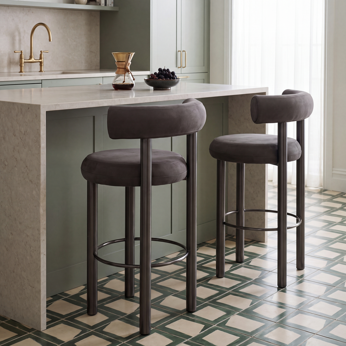 Two upholstered bar stools with dark metal legs and circular footrests placed at a kitchen island in a real kitchen setting.