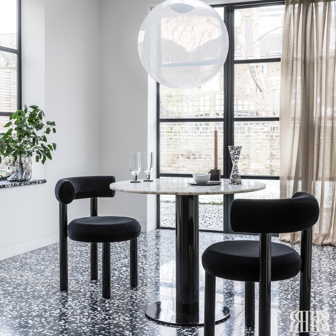 Modern dining area with black chairs and a round table near large windows.