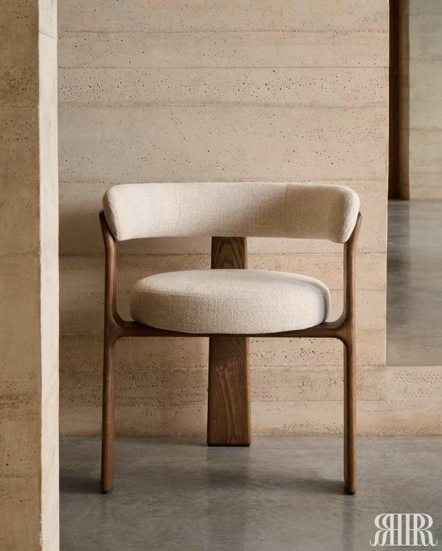 Beige chair with wooden legs against a beige stone wall