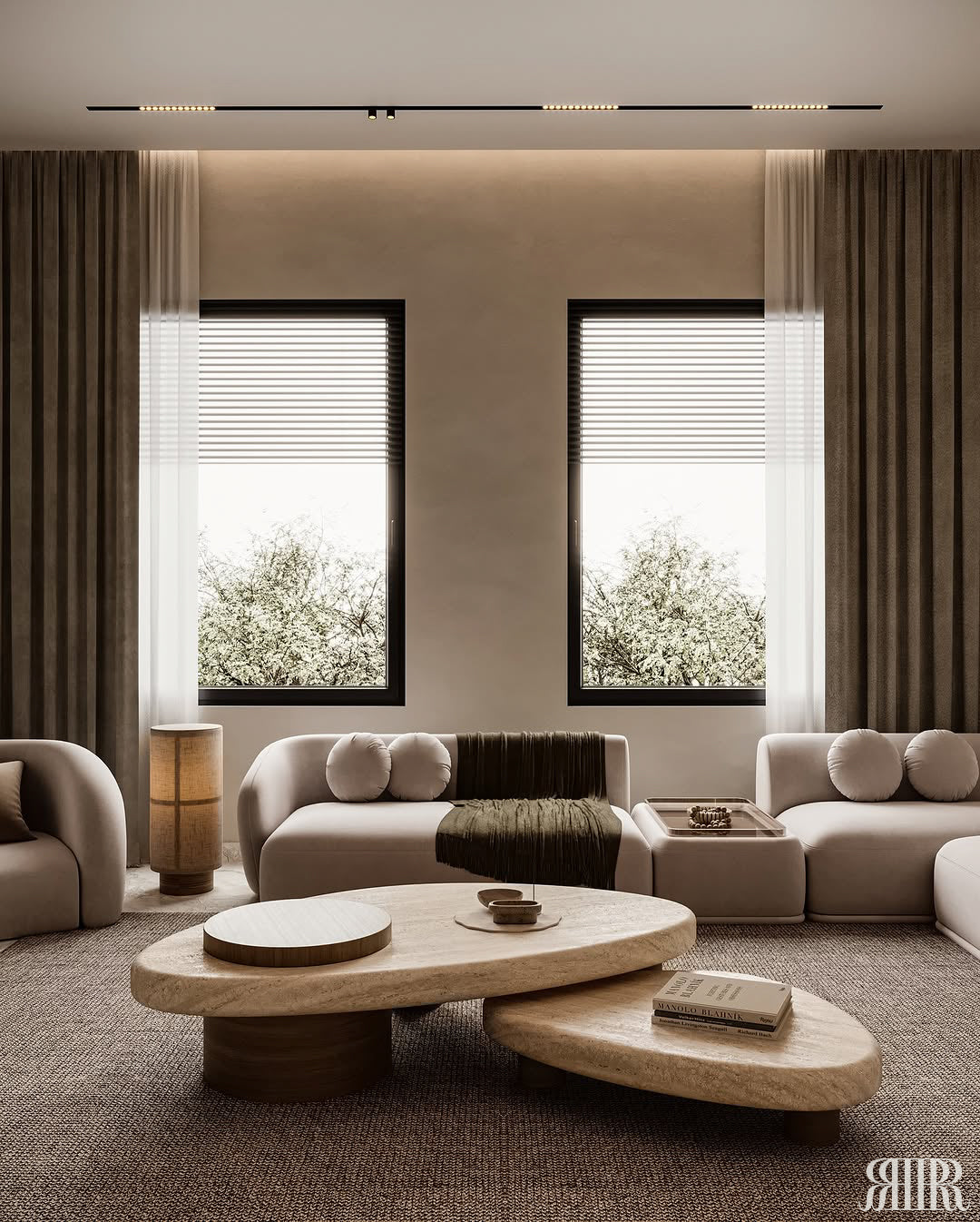 A modern living room interior with two tall windows, sheer and dark drapes, a beige sectional sofa, and two organic-shaped layered coffee tables in a warm neutral palette.
