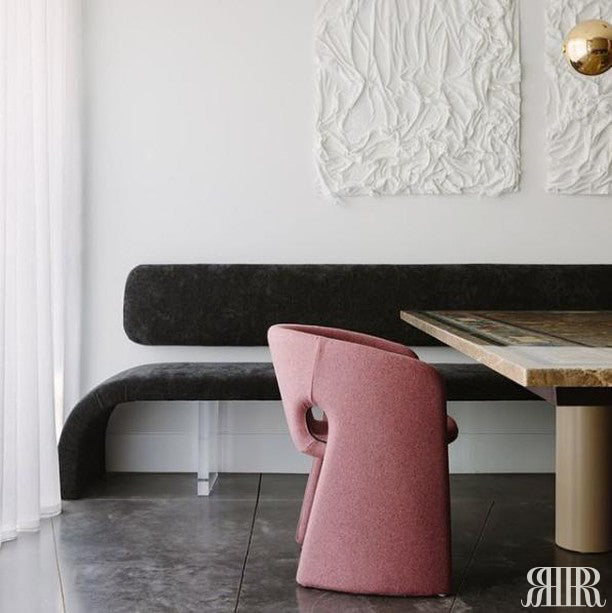 Pink chair in a modern interior setting with a black bench and wooden table.