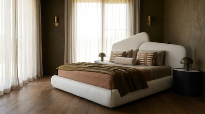 A modern low-profile platform bed with a curved white headboard and footboard, styled with brown and beige bedding in a warm, contemporary bedroom.