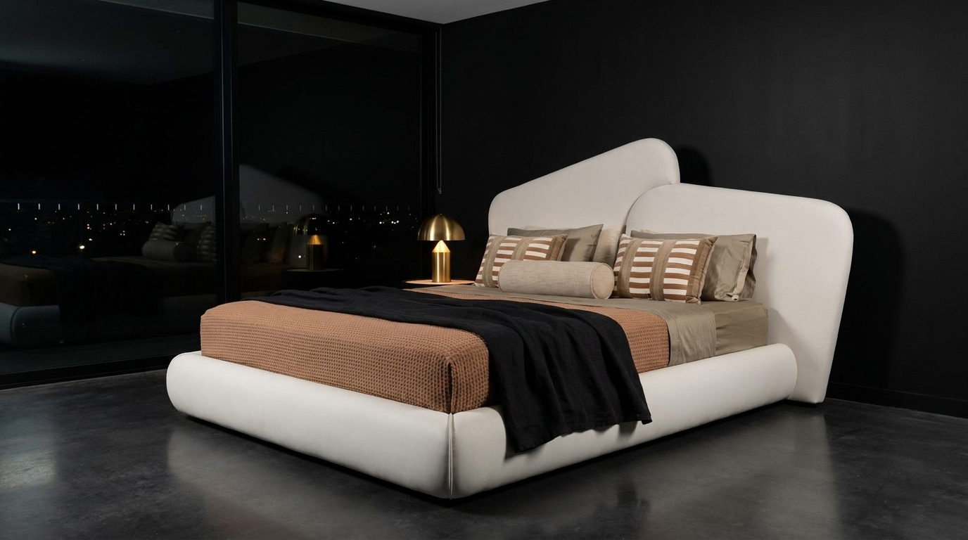A modern low-profile platform bed with a curved, sculptural headboard and footboard in white leather, styled with a textured tan quilt, striped beige pillows, and a black throw blanket, set in a dark, minimalist bedroom.