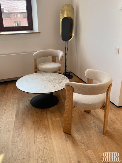 Modern interior with two beige chairs and a round marble table on a wooden floor.