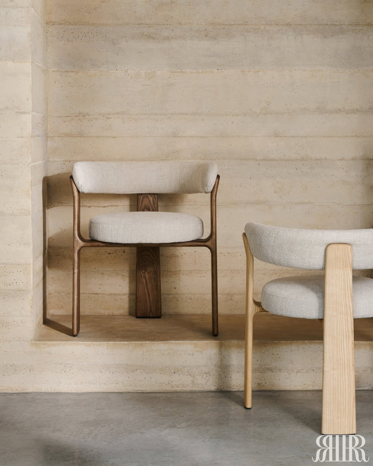 Two chairs with wooden frames and white cushions against a textured beige wall.