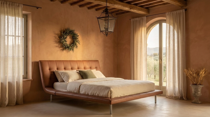 A modern platform bed with a tufted brown leather headboard and matching footboard, styled in a rustic Mediterranean bedroom with terracotta walls, sheer curtains, and a hanging lantern.