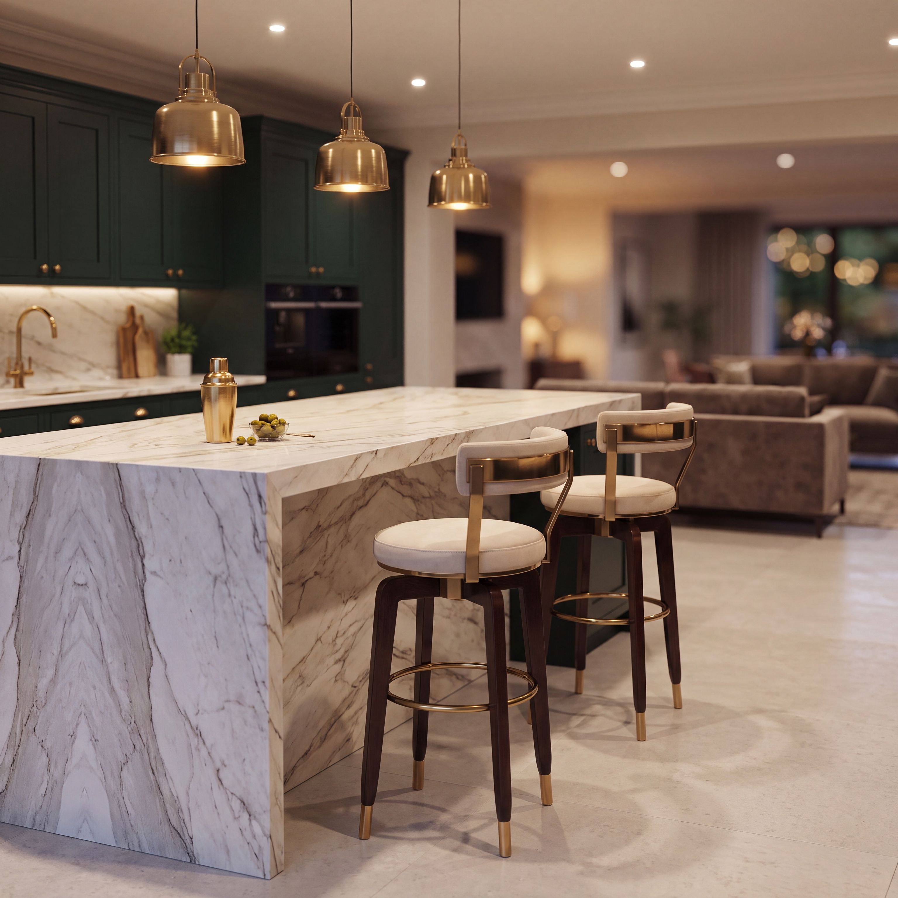 A modern kitchen island with a white marble-look countertop and matching marble base, paired with two bar stools that have cream cushions and gold-toned metal frames. The kitchen features dark green cabinetry, gold pendant lights, and a bright, upscale interior.